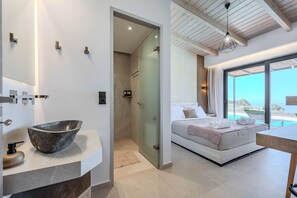 A modern bathroom with a large basin, a shower, and a glass door leading to a bedroom with a bed and a view of the sea. - Rodia Luxury villa ,Sea View Retreat near Plakias (Plakias)
