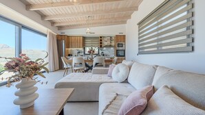 Un salon moderne avec un canapé, un coin repas avec des chaises et une cuisine dotée de meubles en bois et d’une grande fenêtre.