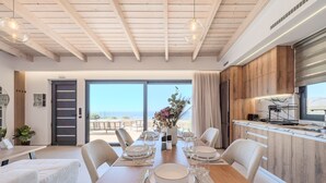 Une cuisine moderne avec des meubles en bois, un coin repas avec une table dressée pour quatre personnes, et une vue sur la plage par la baie vitrée coulissante.