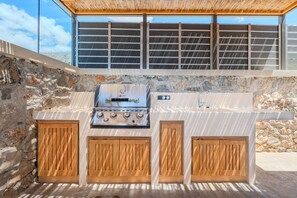 An outdoor kitchen with a built-in grill, wooden cabinets, and a stone wall backdrop. - Rodia Luxury villa ,Sea View Retreat near Plakias (Plakias)