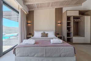 A modern bedroom with a large bed, built-in shelving, a view of a pool, and a wooden ceiling. - Rodia Luxury villa ,Sea View Retreat near Plakias (Plakias)