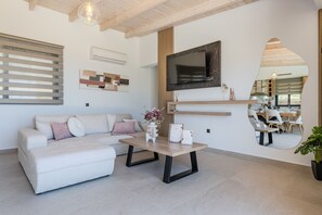 A modern living room with a sofa, coffee table, TV, and a mirror reflecting a dining area. - Rodia Luxury villa ,Sea View Retreat near Plakias (Plakias)