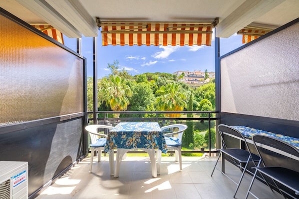 A balcony with a table and chairs, a view of greenery and buildings, and a striped awning. - Le Palme by Wonderful Italy (Sanremo)
