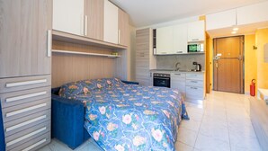 Una habitación compacta con cama, kitchenette pequeña y baño.