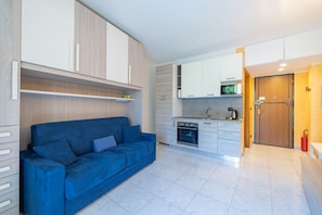 A compact living space with a sofa, kitchenette, and a door leading to another room. - Le Palme by Wonderful Italy (Sanremo)