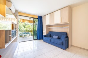 A compact living space with a balcony, a blue sofa, and a sliding glass door leading to a garden. - Le Palme by Wonderful Italy (Sanremo)