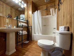 A bathroom with a wooden interior, a white sink, a toilet, and a bathtub. - Scenic Waterfront Cabin with Covered Porch Overlooking Private Pond near Zwolle, Louisiana (Zwolle)