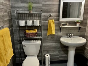 Ein Badezimmer mit Toilette, Waschbecken, Ablagefläche für Toilettenartikel, Spiegel und einem gelben Handtuch.