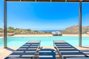Ein Poolbereich mit Liegestühlen und Blick auf den Ozean.