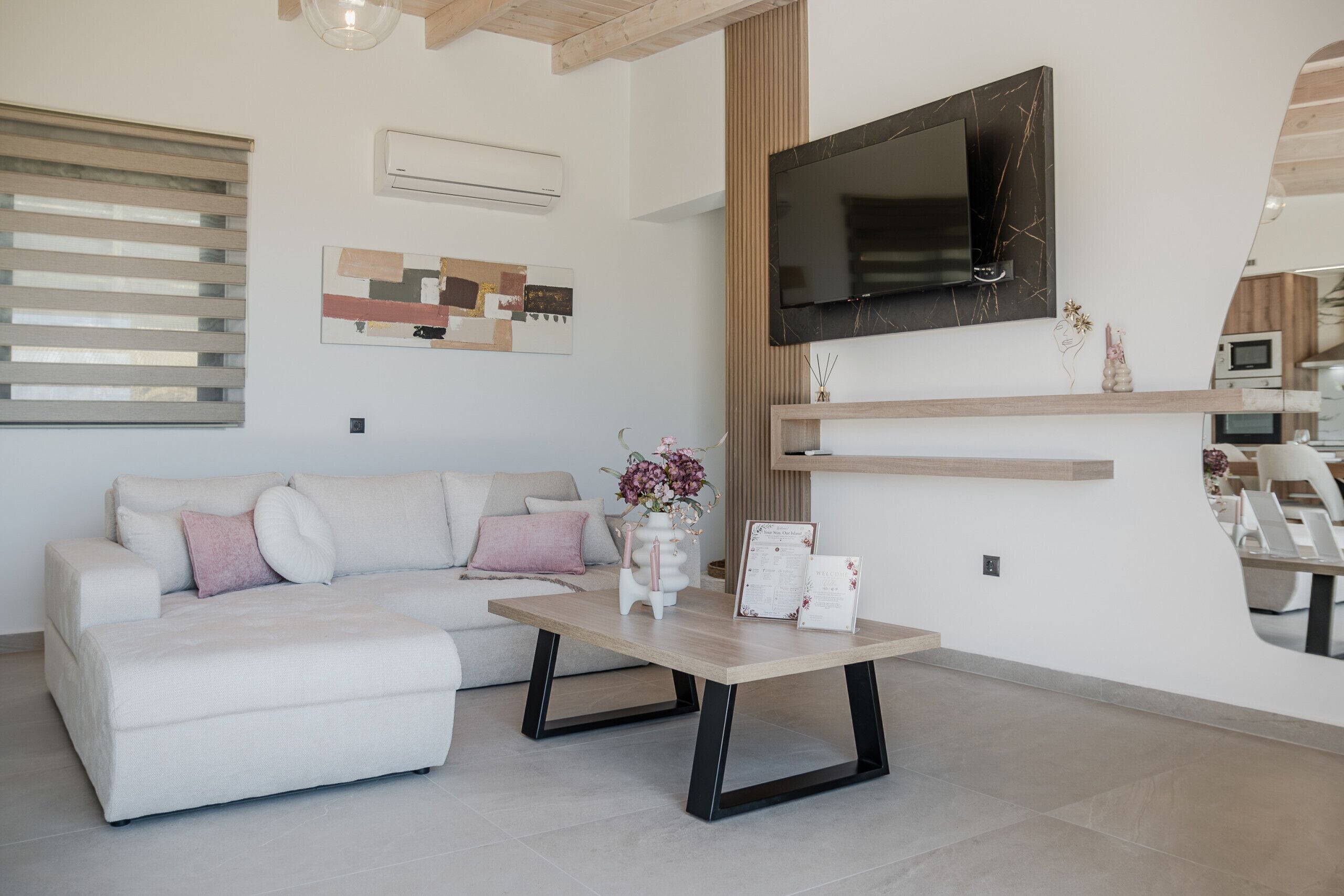 A modern living room with a sofa, coffee table, flat-screen TV, and a wooden shelf.