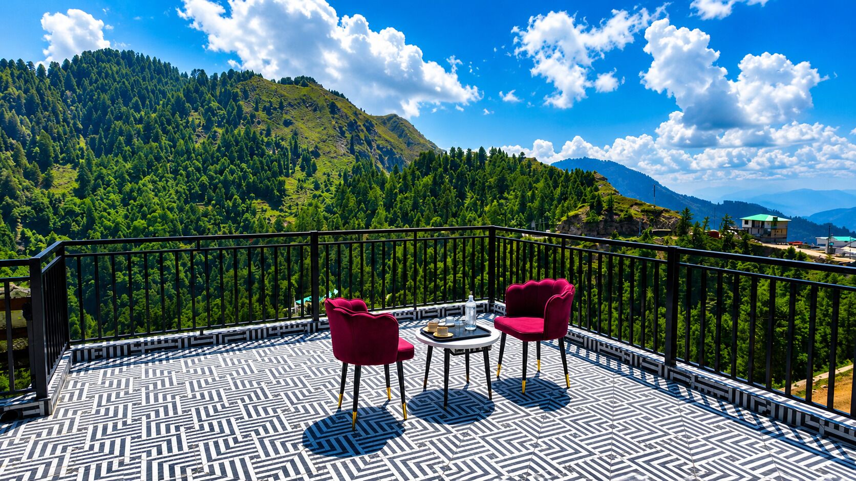 A balcony with patterned flooring, two red chairs, a small table, and a view of a forested mountain.