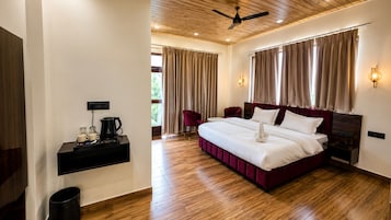 A hotel room with a large bed, a coffee machine, a TV, and a ceiling fan.