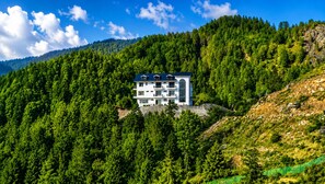 Un edificio moderno de varios pisos con techo plano, rodeado de un bosque denso y colinas.