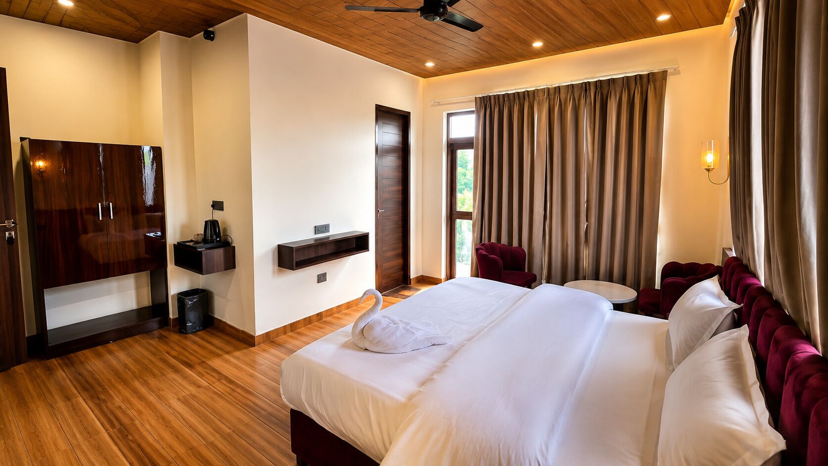 A hotel room with a large bed, a wardrobe, a desk, and a window with curtains.
