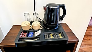 Una estación de café con una cafetera negra, dos tazas color beige, y sobres de azúcar y crema.