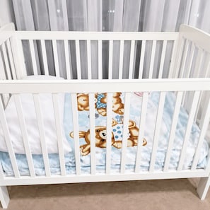 A white crib with a patterned mattress, set against a backdrop of sheer curtains. - Stylish Apartment Sydney Olympic Park Free parking (Sydney Olympic Park)