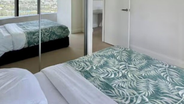 Un dormitorio con un gran ventanal corredero que da a un balcón, una cama con colcha estampada y un armario con puerta espejo corredera.