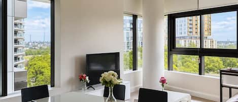 A modern dining area with a white table, black chairs, and a flat-screen TV.