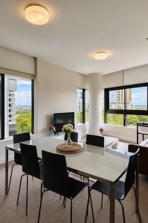 A modern dining area with a white table, black chairs, and a flat-screen TV. - Stylish Apartment Sydney Olympic Park Free parking (Sydney Olympic Park)