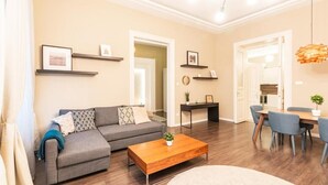 A living room with a sofa, coffee table, and dining area with chairs. There are picture frames on shelves and a hanging light fixture. - Spacious Luxury apartment at the heart of Budapest (Budapest)