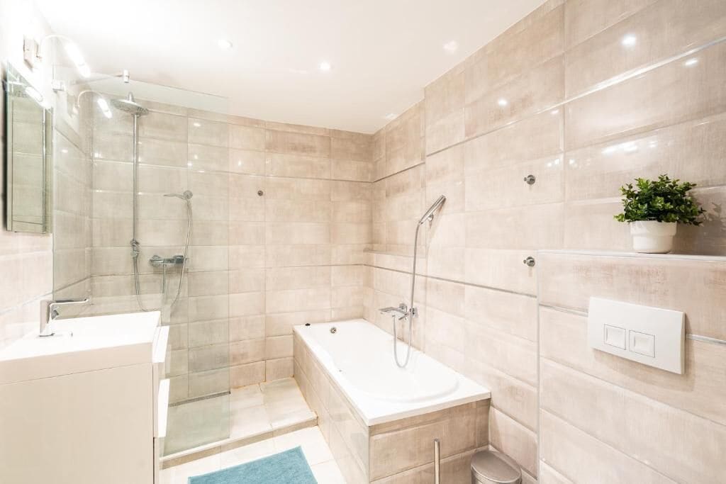 Une salle de bain moderne avec une douche à parois de verre, une baignoire, un lavabo et une plante en pot.