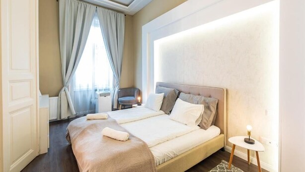 A double bed with a headboard, a bedside table, a chair, and a window with curtains. - Spacious Luxury apartment at the heart of Budapest (Budapest)