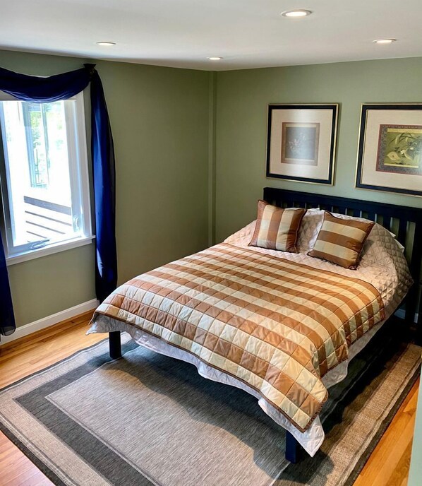 Un dormitorio con cama, ventana con cortinas y dos cuadros en la pared.