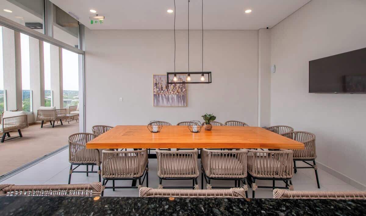 Une salle de conférence dotée d’une grande table en bois, de chaises en osier, d’un téléviseur fixé au mur et offrant une vue sur la ville grâce à de grandes fenêtres.