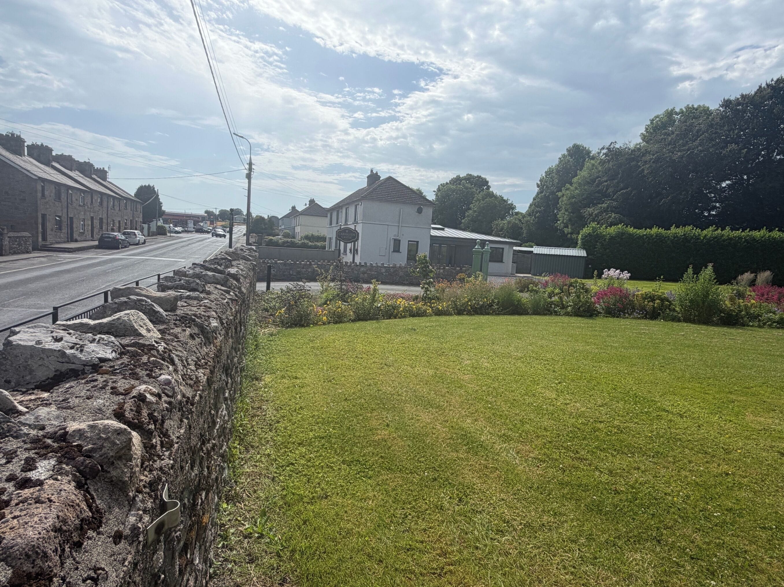 A rural street with stone walls, a grassy lawn, and houses with traditional architecture.