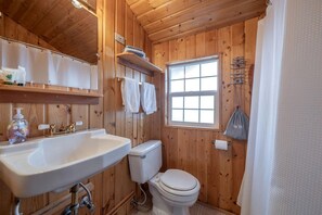 Een houten badkamer met een wastafel, toilet en raam.