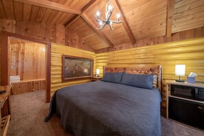 Een blokhutkamer met een bed, een schilderij, een kroonluchter en een nachtkastje met een lamp.