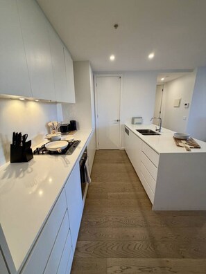 A modern kitchen with white cabinetry, a central island, and a wooden floor. - Rooftop Infinity Pool & Bay Views Pet Friendly (St Kilda)
