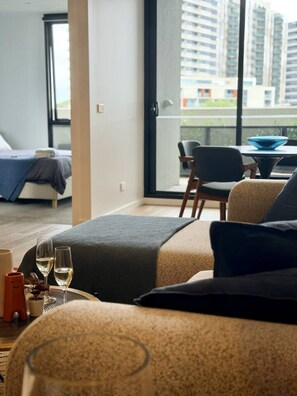 A modern living room with a sofa, a dining table, and a balcony with a view of high-rise buildings. - Rooftop Infinity Pool & Bay Views (St Kilda)