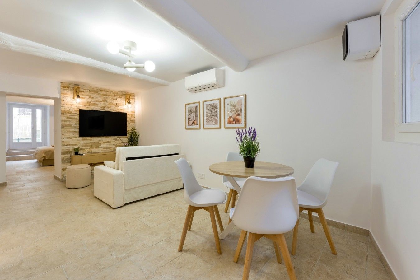 Un salon moderne comprenant un canapé, une table à manger avec des chaises, un téléviseur à écran plat fixé à un mur en pierre et un ventilateur de plafond.