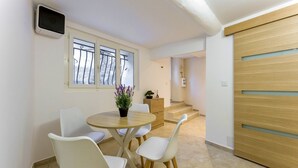 A dining area with a round table and four chairs, a potted plant, and a view through a window with metal bars. - Petit Pont d'Avignon — apartment with terrace & A/C (Villeneuve-lès-Avignon)