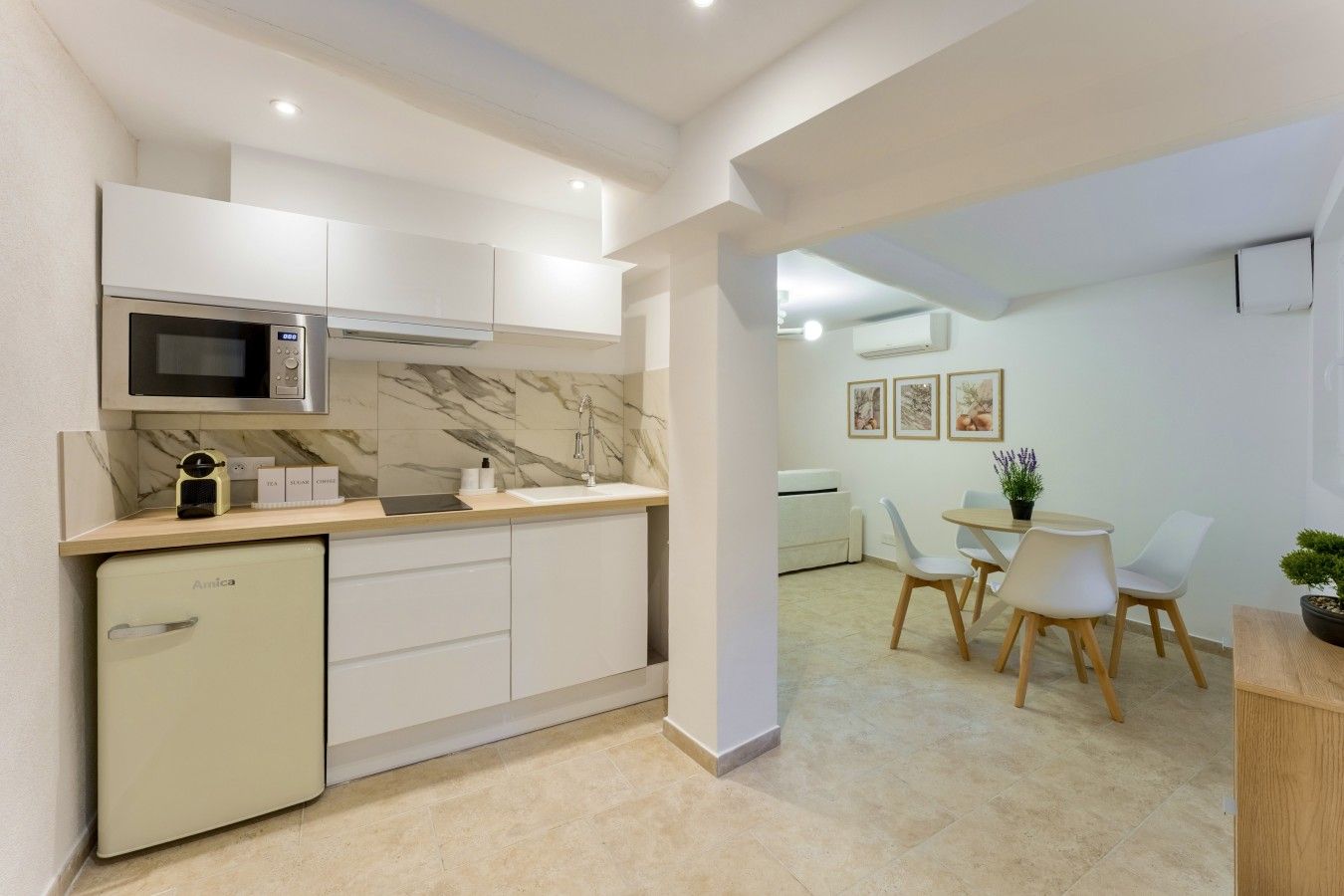Cocina moderna con microondas, lavamanos y un refrigerador compacto. Hay una zona de comedor con mesa y sillas.