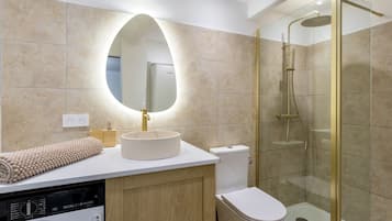 A modern bathroom with a round sink, a toilet, a glass-enclosed shower, and a built-in washing machine.