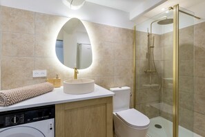 Un bagno moderno con un lavabo rotondo, un WC, una cabina doccia in vetro e una lavatrice a incasso.