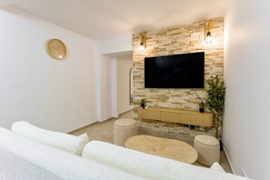 Una sala moderna con una televisión de pantalla plana montada en una pared de piedra, un sofá, dos otomanas y un reloj en la pared.