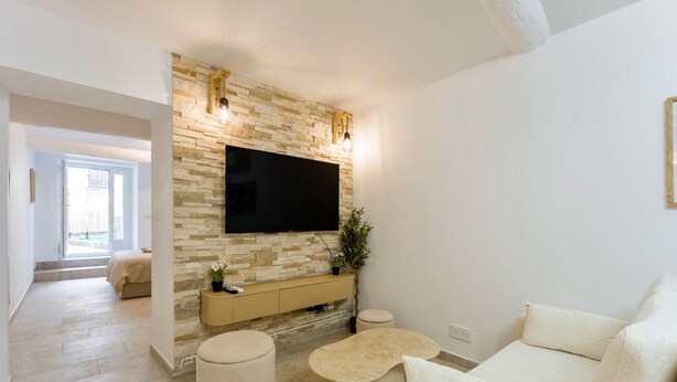 A modern living room with a stone wall, a flat-screen TV, a sofa, and a coffee table. - Petit Pont d'Avignon — apartment with terrace & A/C (Villeneuve-lès-Avignon)