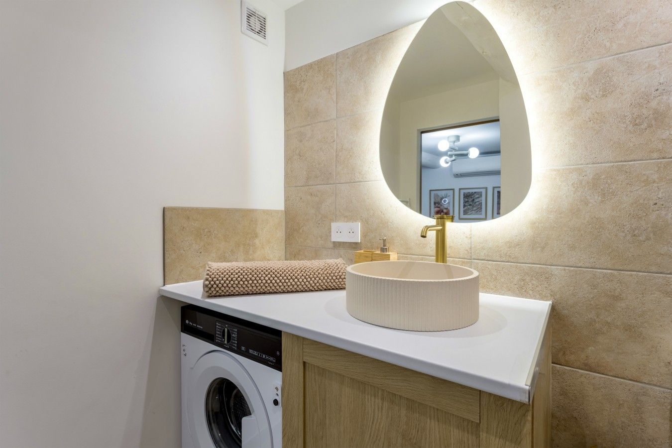 Une salle de bain équipée d’un lave-linge, d’un évier avec un robinet doré et d’un miroir à cadre ovale.