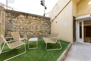 Un patio con dos sillones de descanso y una mesa pequeña, un muro de piedra y la entrada de un edificio.