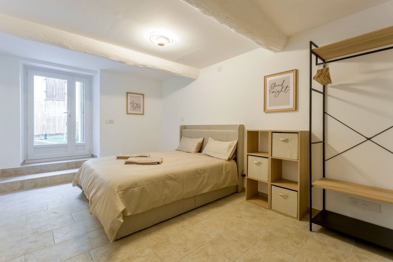 Un dormitorio con cama, mesita de noche, armario y ventana.