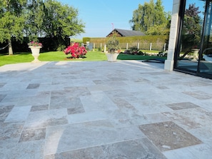 Un patio empedrado con baldosas de piedra, rodeado de vegetación y un edificio con entrada de cristal.