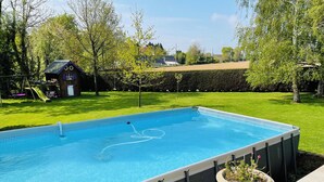 Piscina rectangular con borde de azulejos, rodeada de césped y árboles.