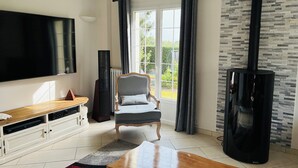 Una sala de estar con televisor de pantalla plana, una mesa de centro de madera, un sillón gris, un altavoz negro y una chimenea negra.