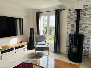 Ein Wohnzimmer mit Flachbildfernseher, einem Holztisch, einem grauen Sessel, einem schwarzen Lautsprecher und einem schwarzen Kamin.