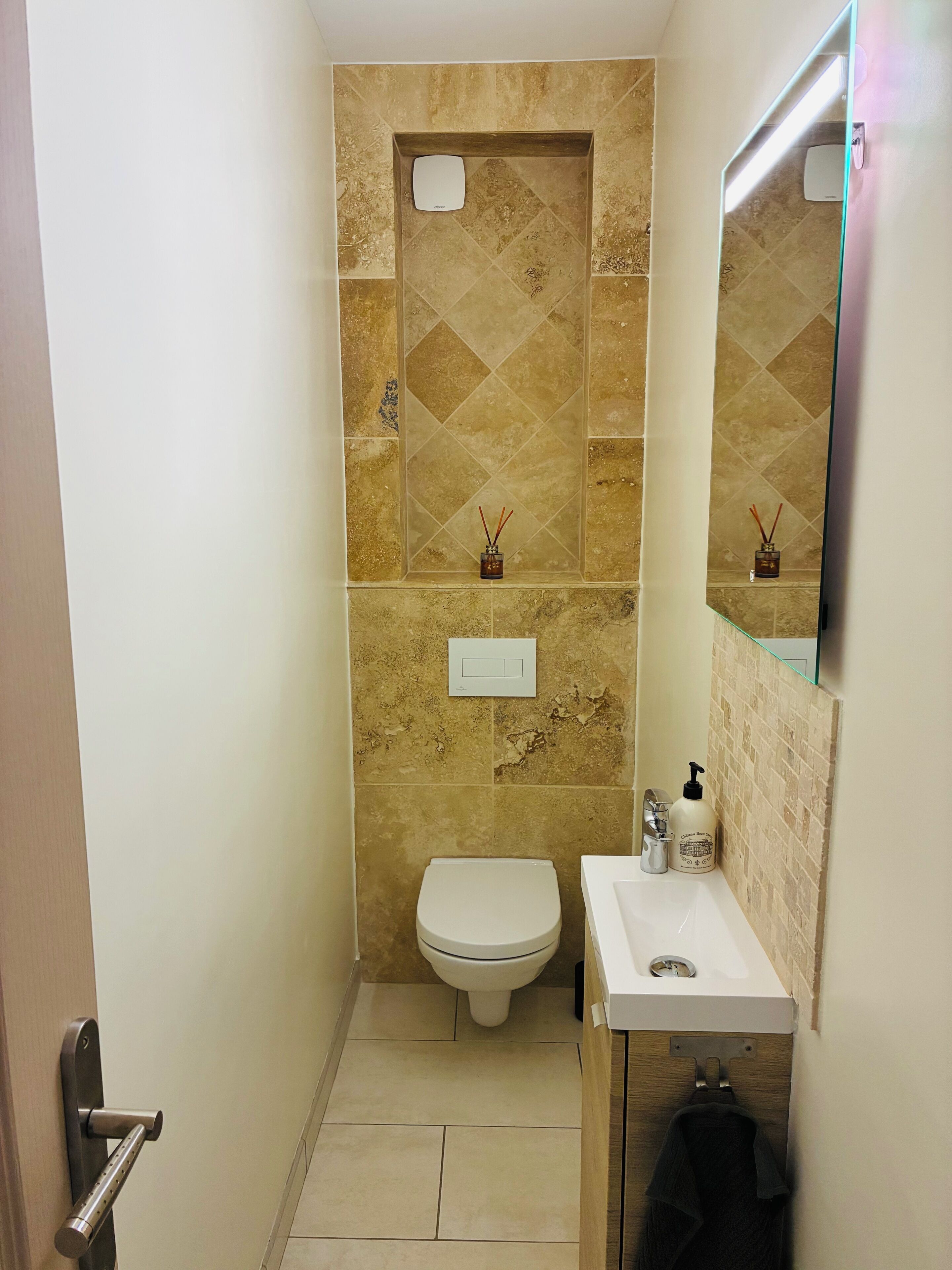 A bathroom with a toilet, sink, mirror, and decorative tiles.