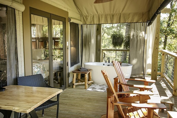 A wooden deck with a table and chairs, a bathtub, and a view of trees.