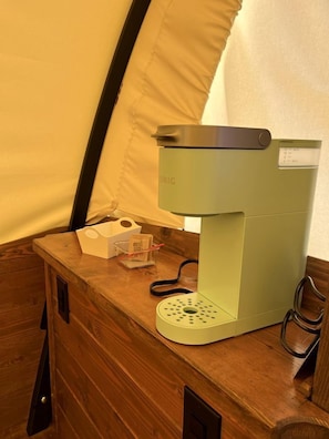 Une machine à café compacte et moderne, posée sur une table en bois dans une pièce qui ressemble à une tente.